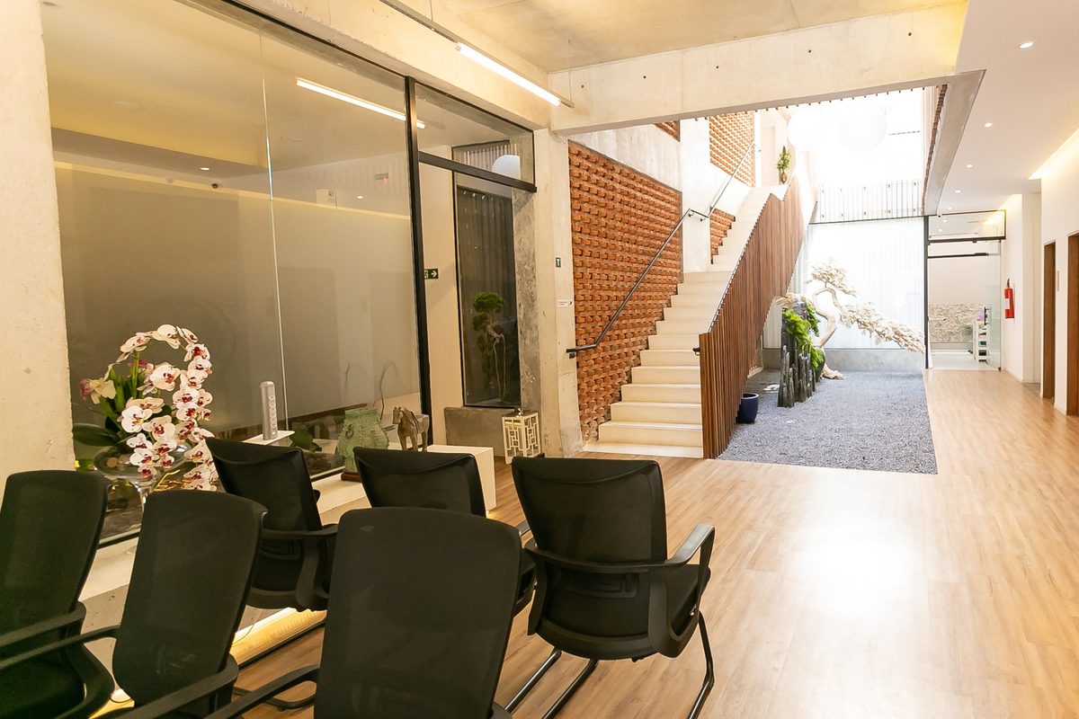 Sala de espera da clínica com vista para o átrio: cadeiras, escada, parede de tijolos vazados e ripado de madeira