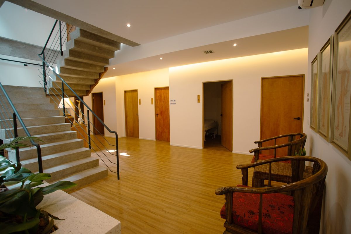 Hall da clínica com a escada, as portas dos consultórios e cadeiras de madeira