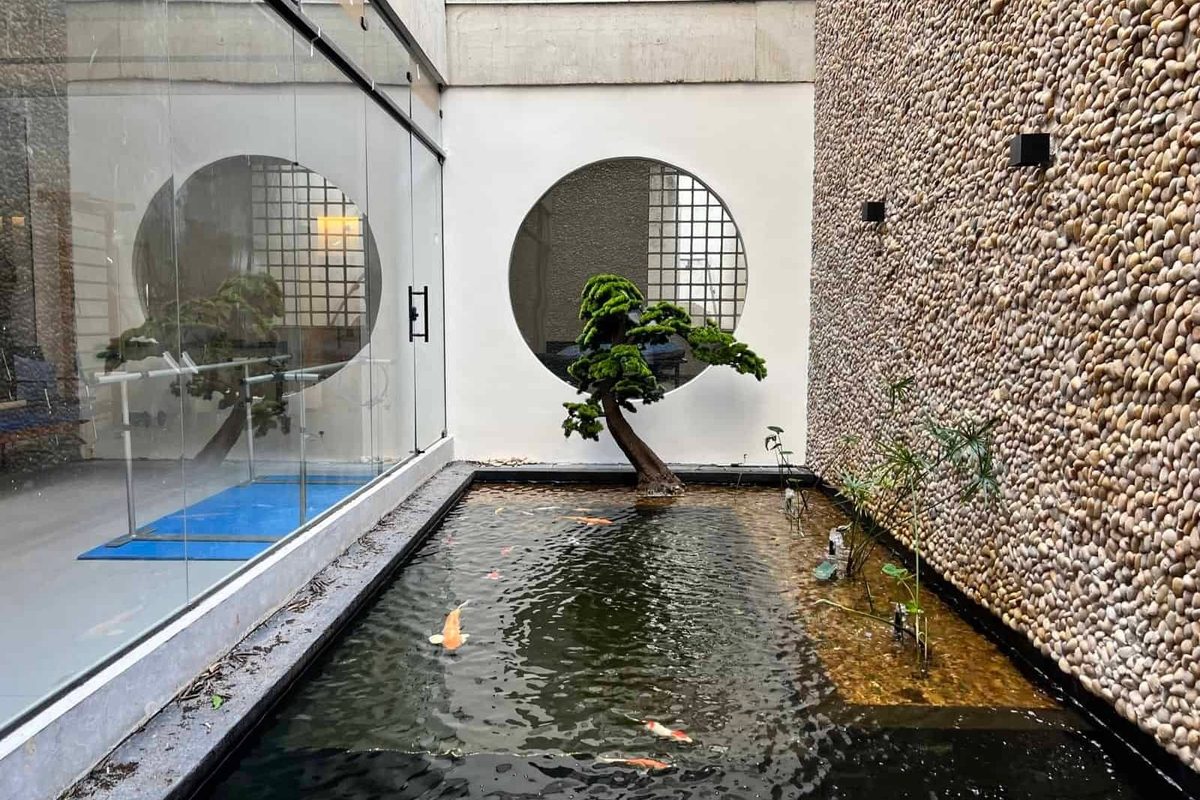 Jardim interno da clínica com espelho d'água, janela redonda e bonsai