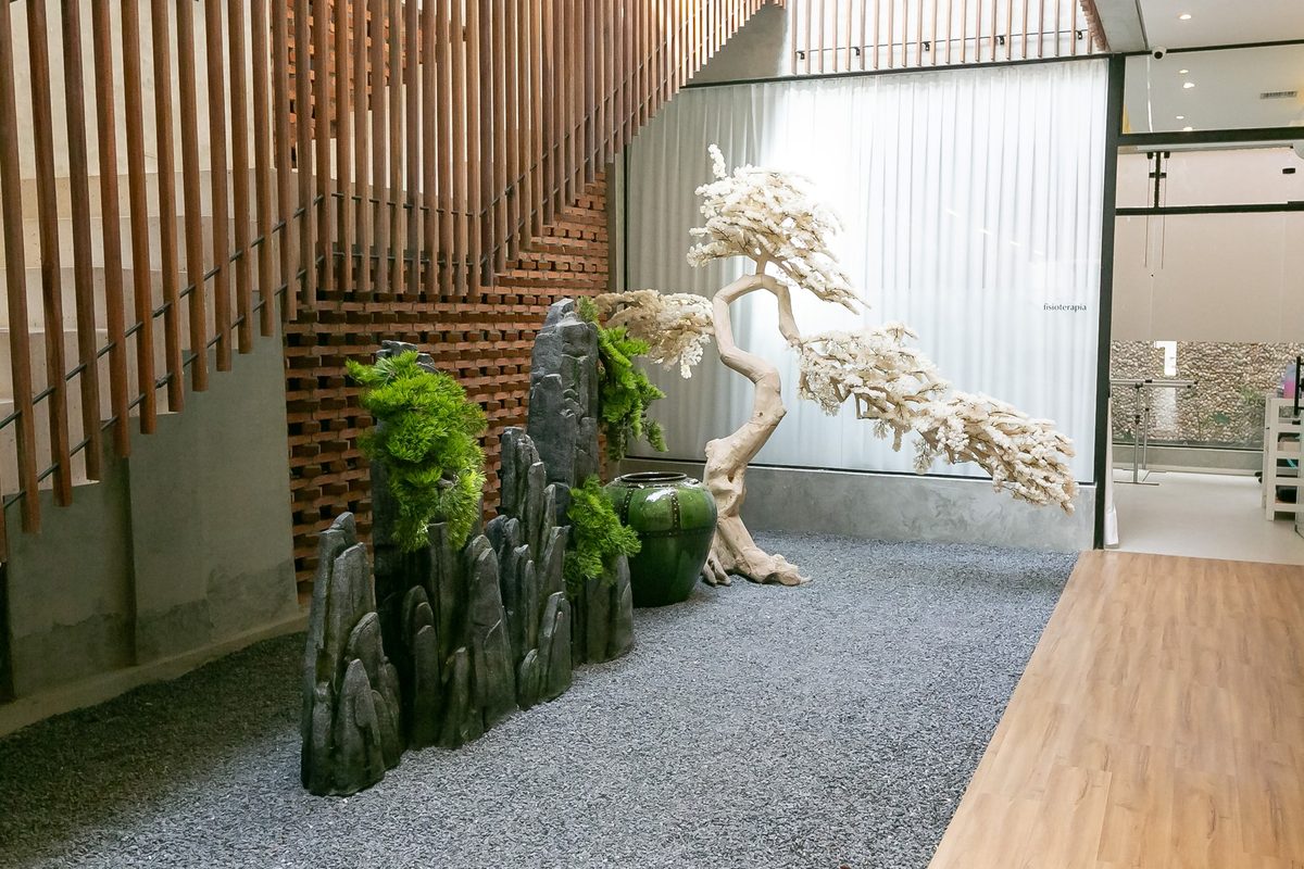 Jardim interno da clínica com pedras, árvore ornamental branca e ripas de madeira