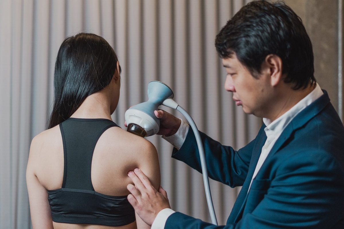 Dr. Marcus Yu Bin Pai aplica ondas de choque focal no ombro de uma pessoa vista de costas