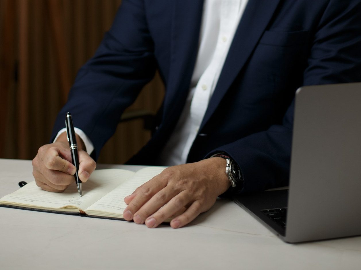 Mãos do médico escrevendo com caneta em um caderno aberto sobre a mesa
