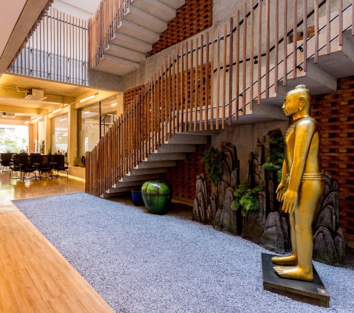 Hall da clínica com estátua dourada de acupuntura, escada e jardim interno