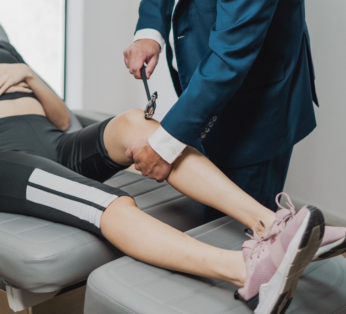 O médico testa o reflexo patelar com um martelo de reflexos em uma pessoa deitada na maca