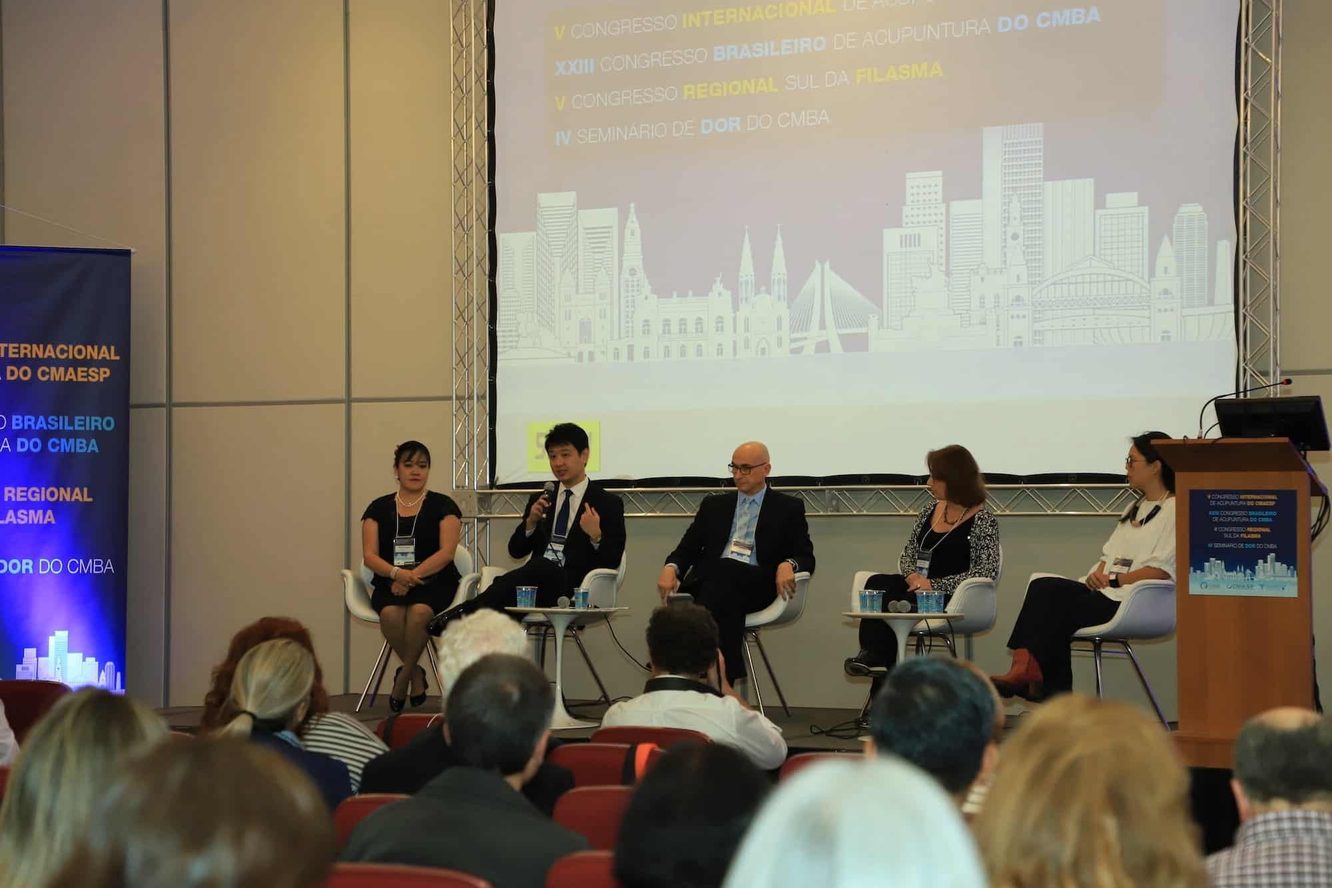 Mesa-redonda do V Congresso Internacional de Acupuntura do CMAeSP e XXIII Congresso Brasileiro de Acupuntura do CMBA: cinco pessoas sentadas no palco, entre elas o Dr. Marcus Yu Bin Pai, com a plateia de costas em primeiro plano