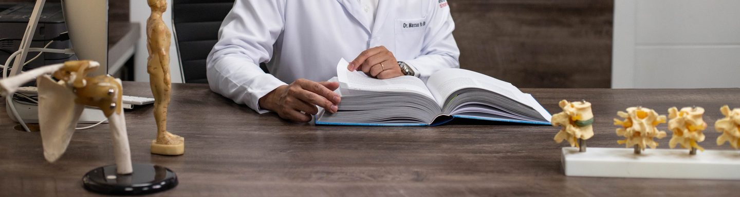 Mãos do médico folheando um livro aberto sobre a mesa do consultório