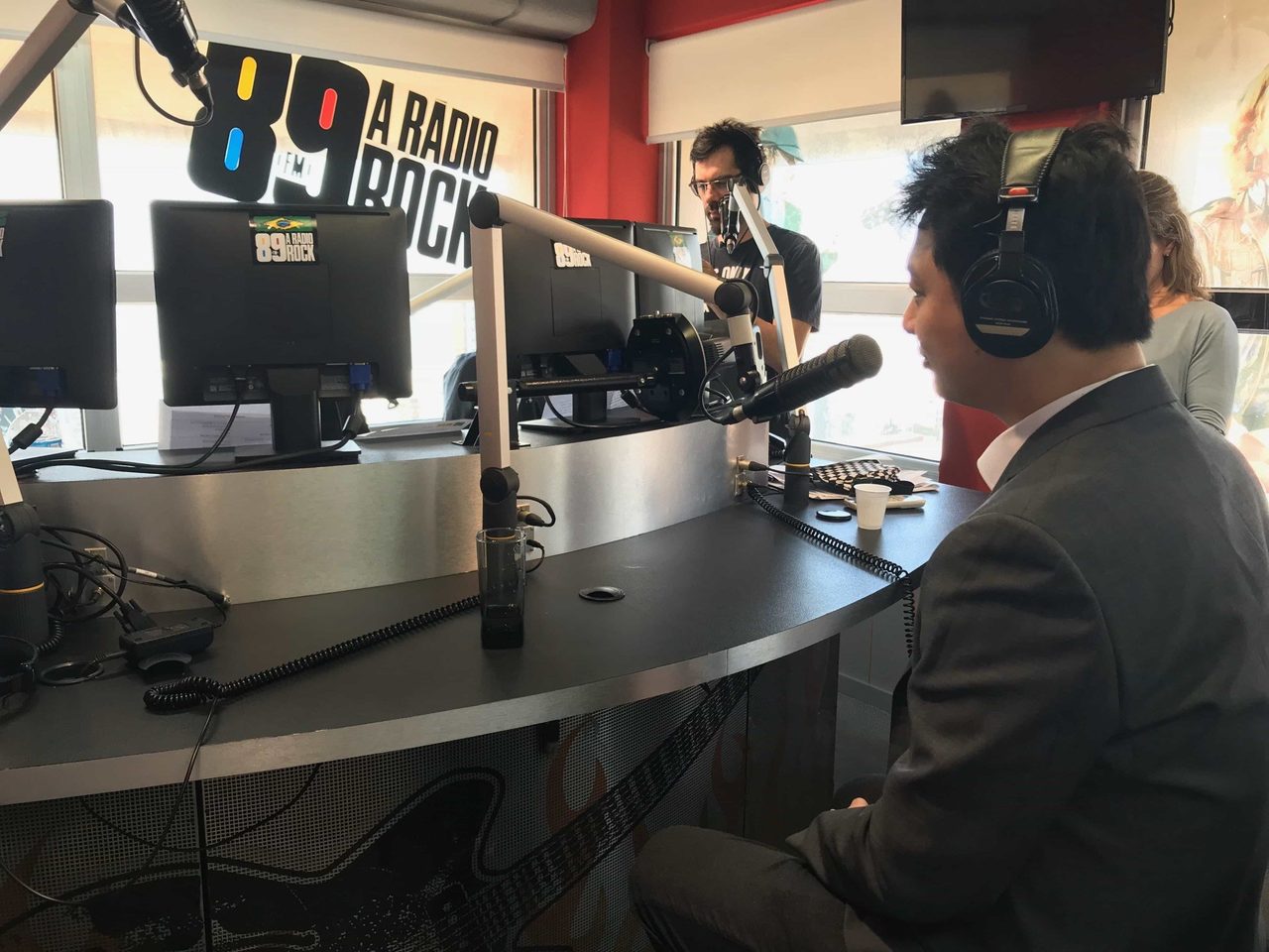 Entrevista em estúdio de rádio com a participação do Dr. Marcus Yu Bin Pai: três pessoas em torno da bancada com microfones, uma delas de fones de ouvido em primeiro plano