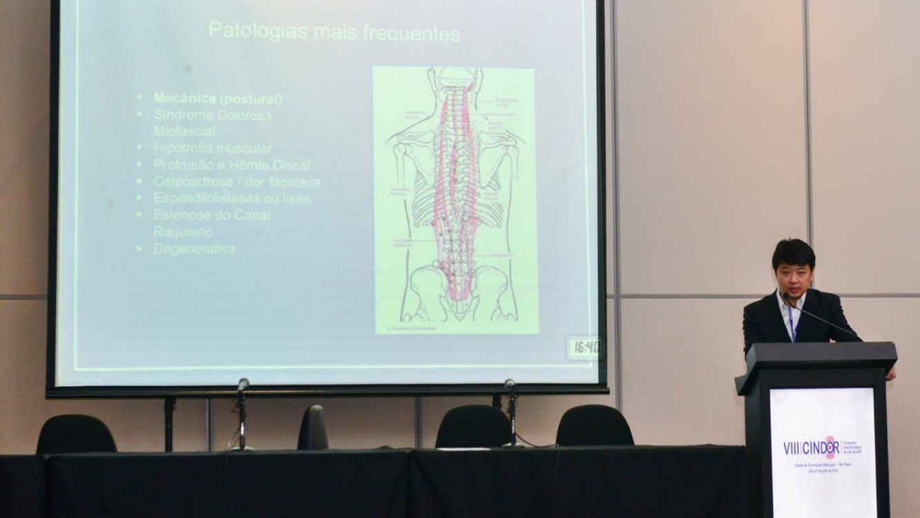 Dr. Marcus Yu Bin Pai fala no púlpito do VIII CINDOR, com slide sobre as patologias mais frequentes da coluna projetado no telão