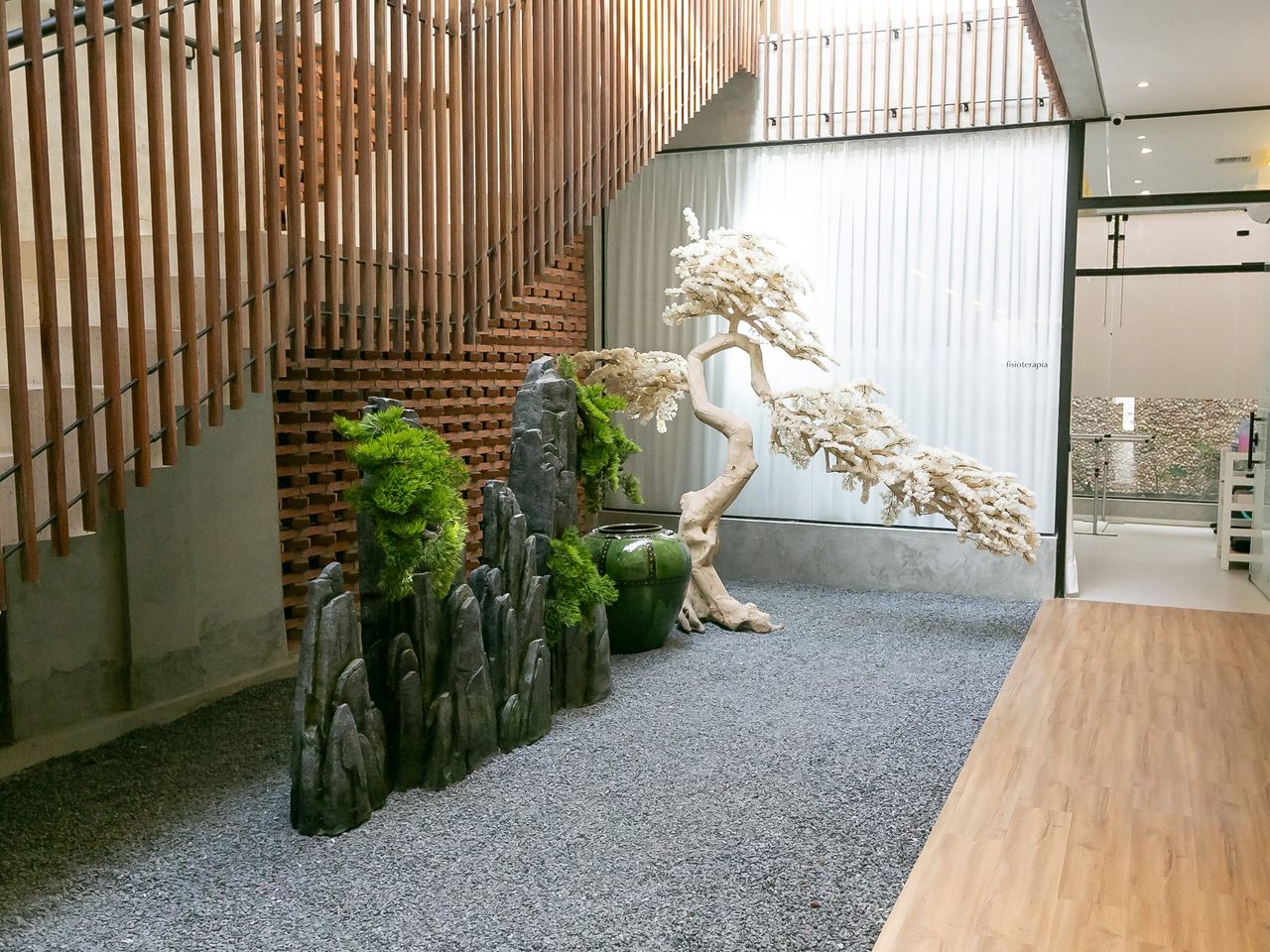 Jardim interno da clínica, com pedras, árvore ornamental branca e ripas de madeira